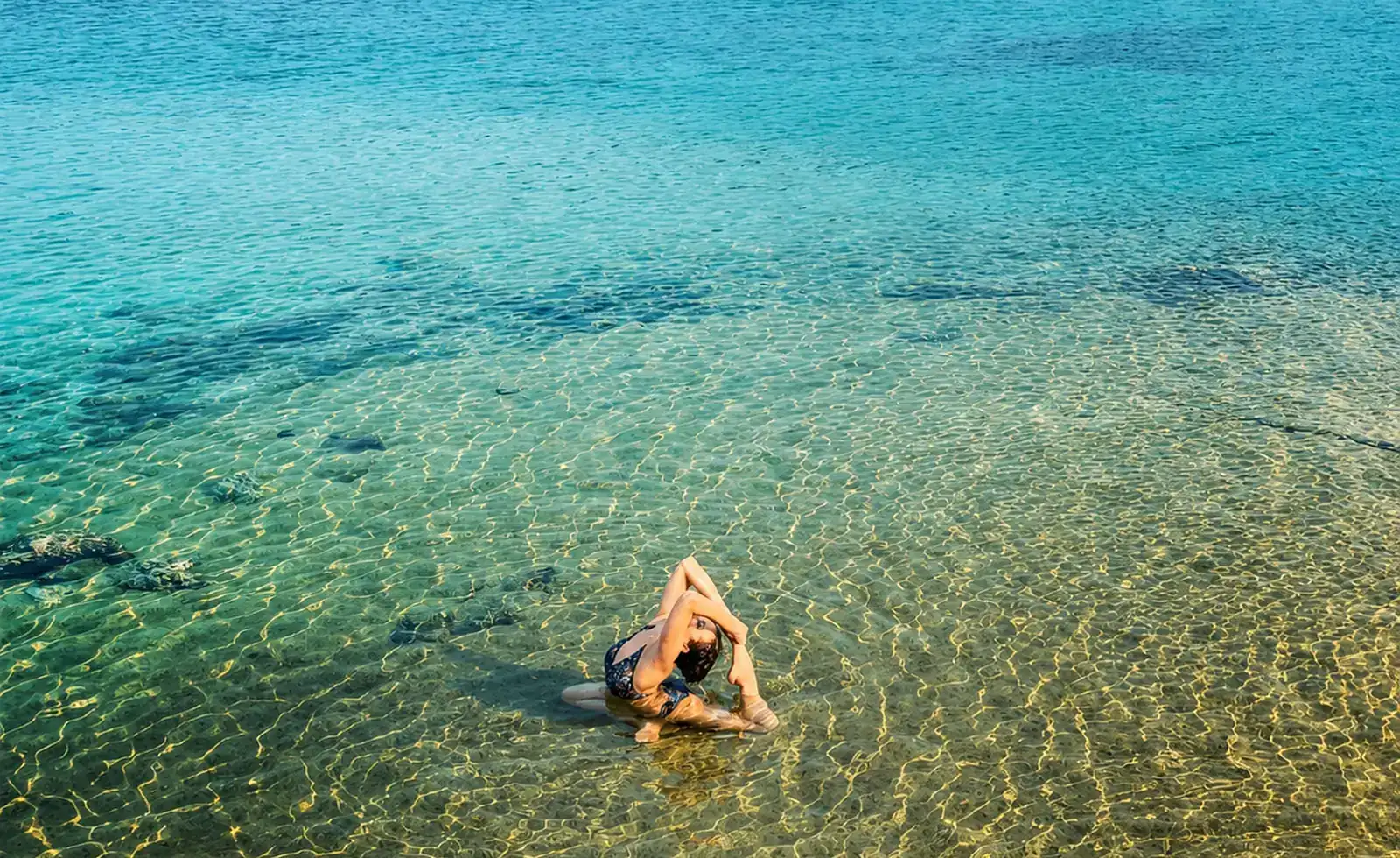 Woman practising yoga in the crystal-clear shallow water of Koh Mak, Thailand, with a palm-fringed beach in the background