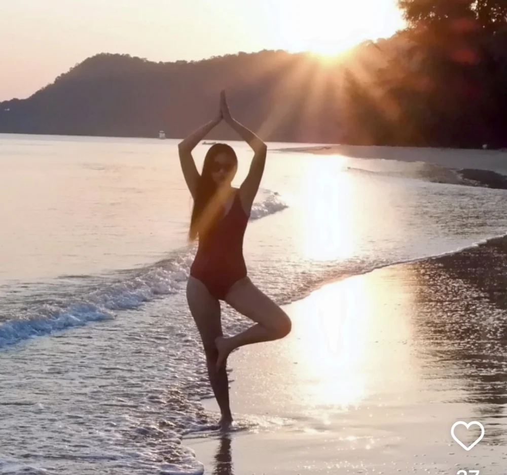 Woman practising yoga tree pose on a quiet Koh Mak beach at golden sunset