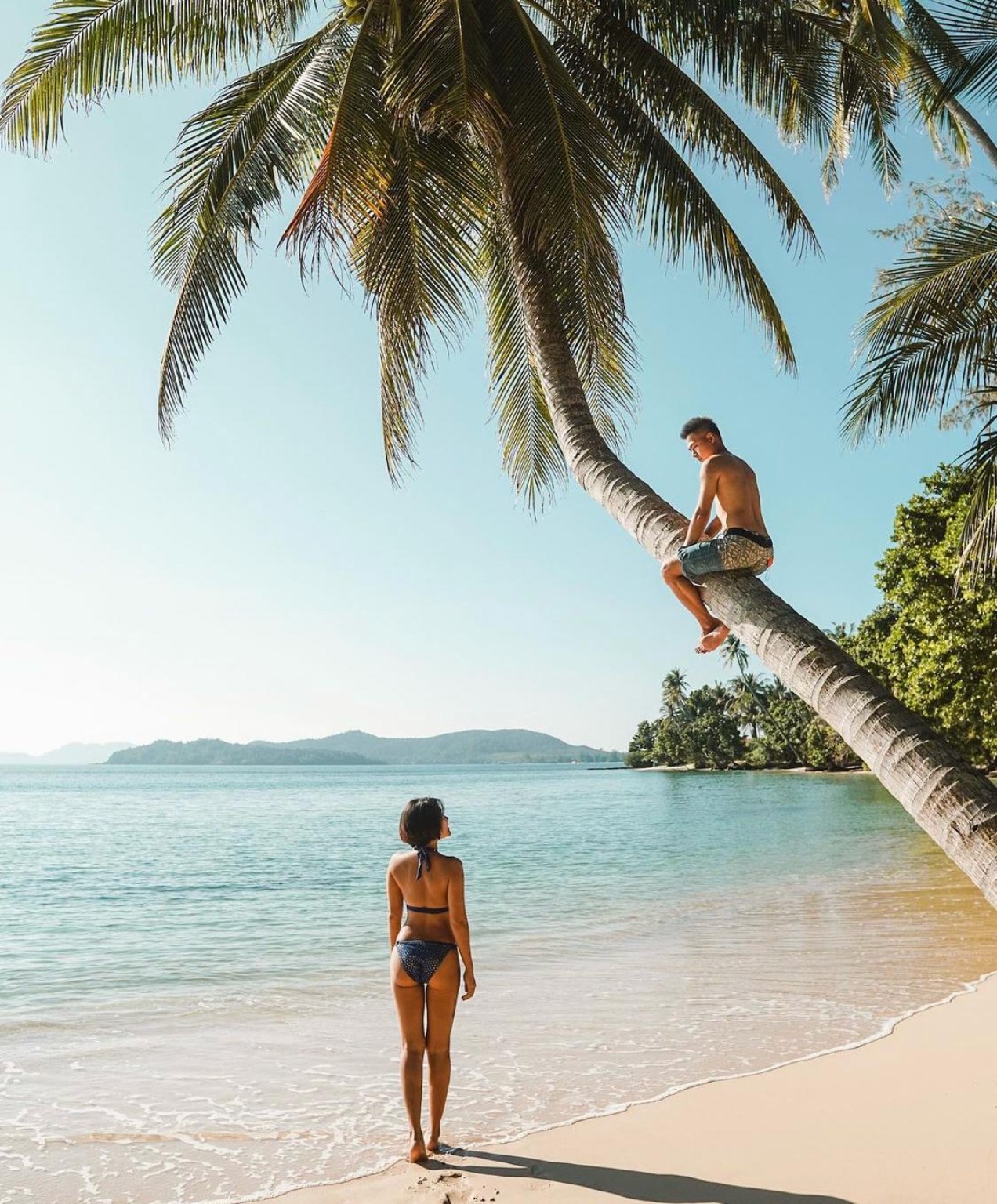 Couple relaxing under a leaning coconut palm on a quiet Koh Mak beach