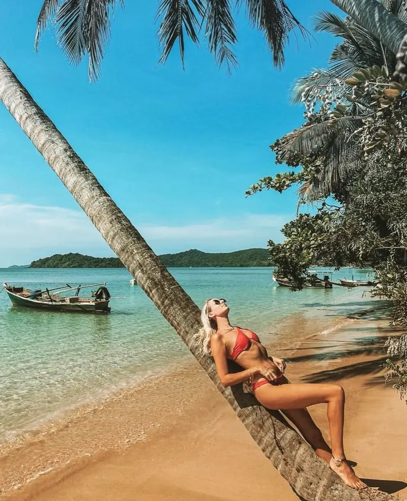 Woman relaxing on a leaning palm tree over turquoise water at a quiet Koh Mak beach